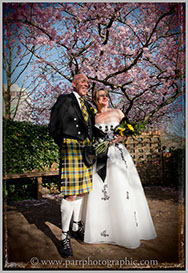 Bride and groom under flowering tree. The groom wears a kilt